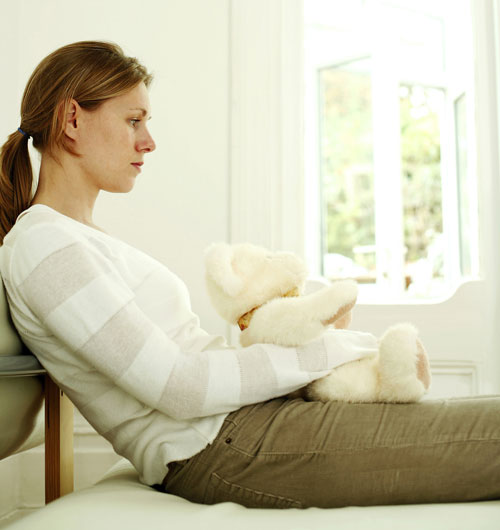 Sad and disappointed woman hugging teddy bear while daydreaming