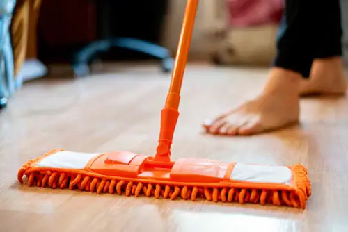 single man holding a mop and cleaning the laminate floor at home