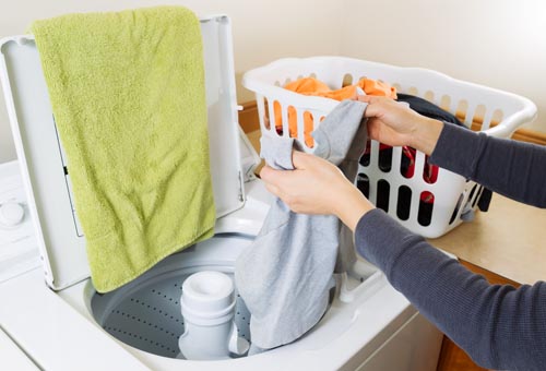 Horizontal photo female hands putting dirty laundry into washing machine
