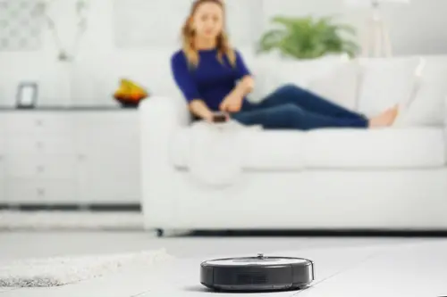 Robotic vacuum cleaner cleaning the room while woman resting on sofa