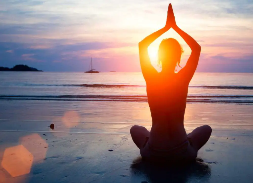 Woman meditating on the beach at sunset