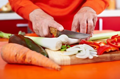 Senior woman hands chopping vegetables on a wooden board in the kitchen