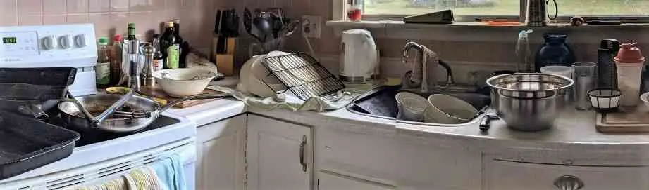 Image of kitchen counter covered in dirty dishes and kitchen sink full of dirty dishes and stove top covered in dirty pots and pans