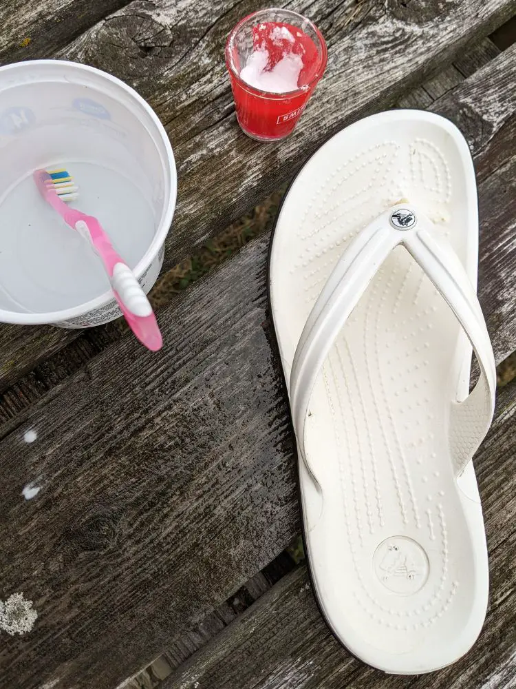 Image of a clean white flip flop on wood deck with dish of water, toothbrush and dish of baking soda 