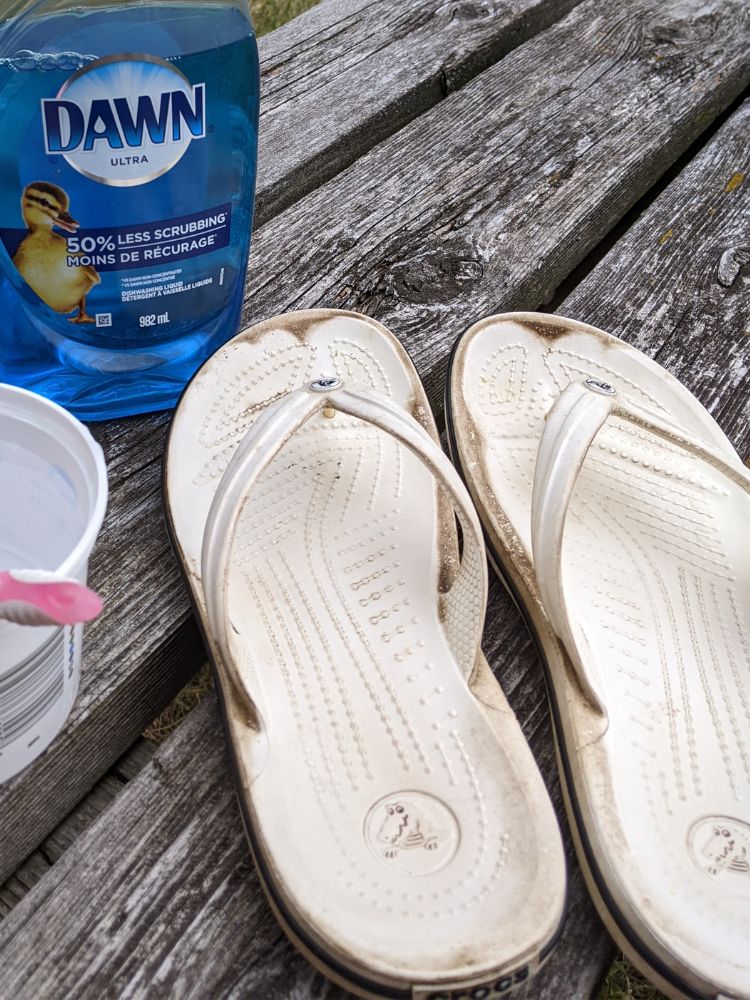 Stained white flip flops on deck with Dawn dish soap, water and a toothbrush for scrubbing