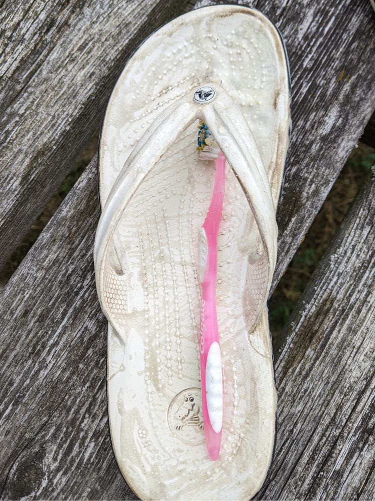 Image of a sudsy dirty white flip flop after being scrubbed with dish soap and toothbrush
